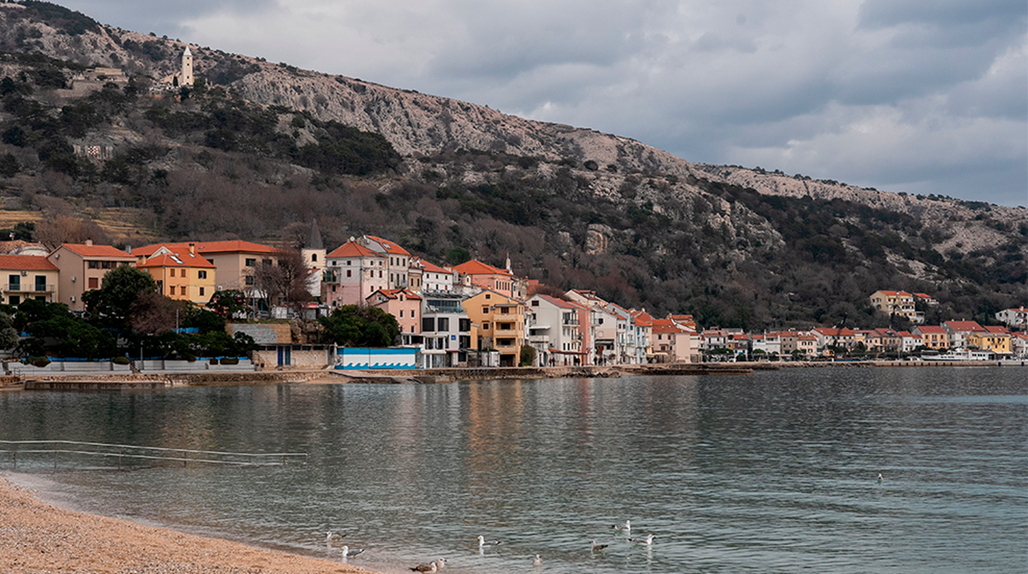 Scenic seaside view of Krk, Croatia with coastal buildings and an overcast sky.