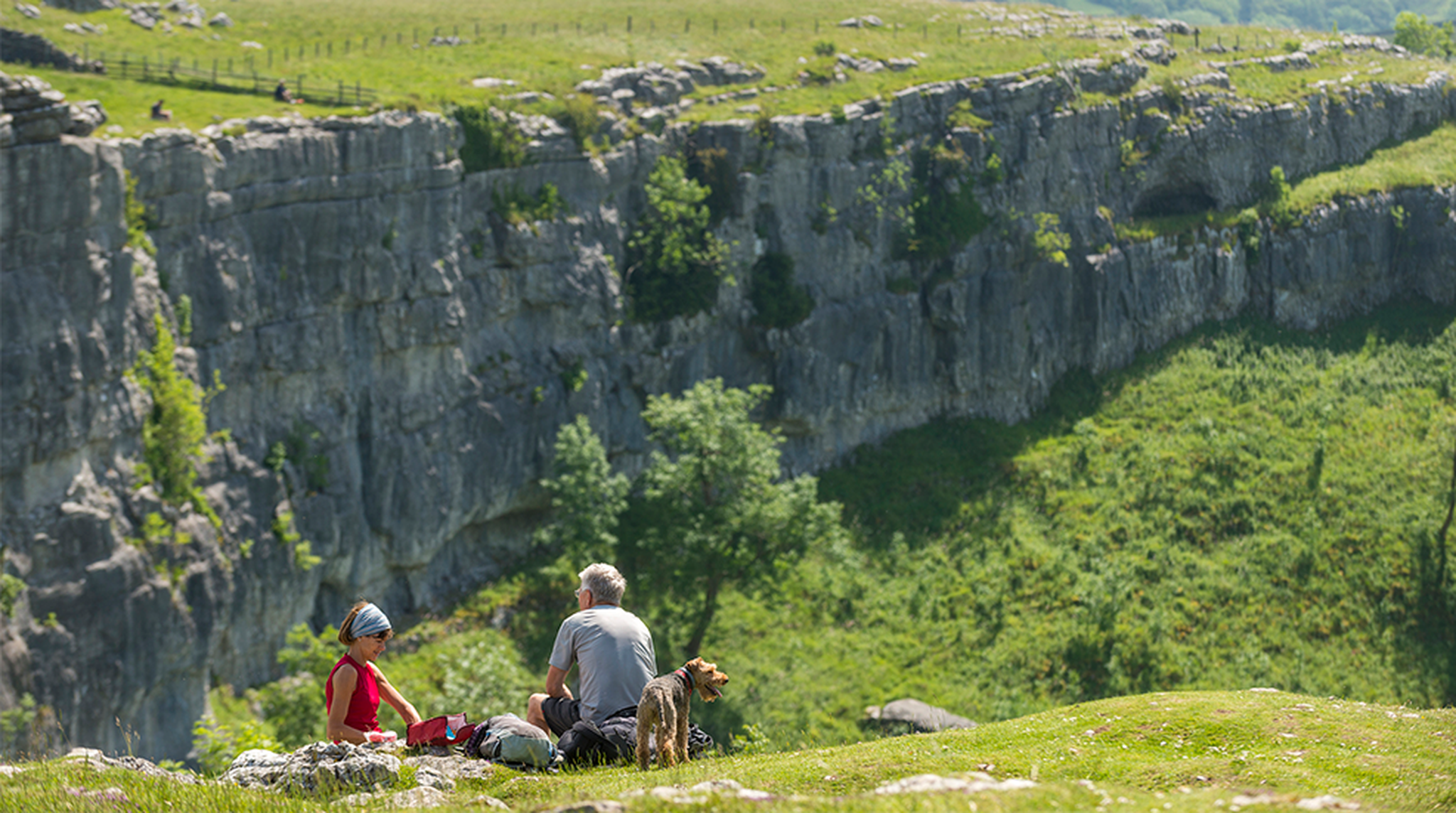 A couple hiking the Pennine Way stop for a picnic at Malham Cove in the Yorkshire Dales National Park with their Welsh Terrier dog