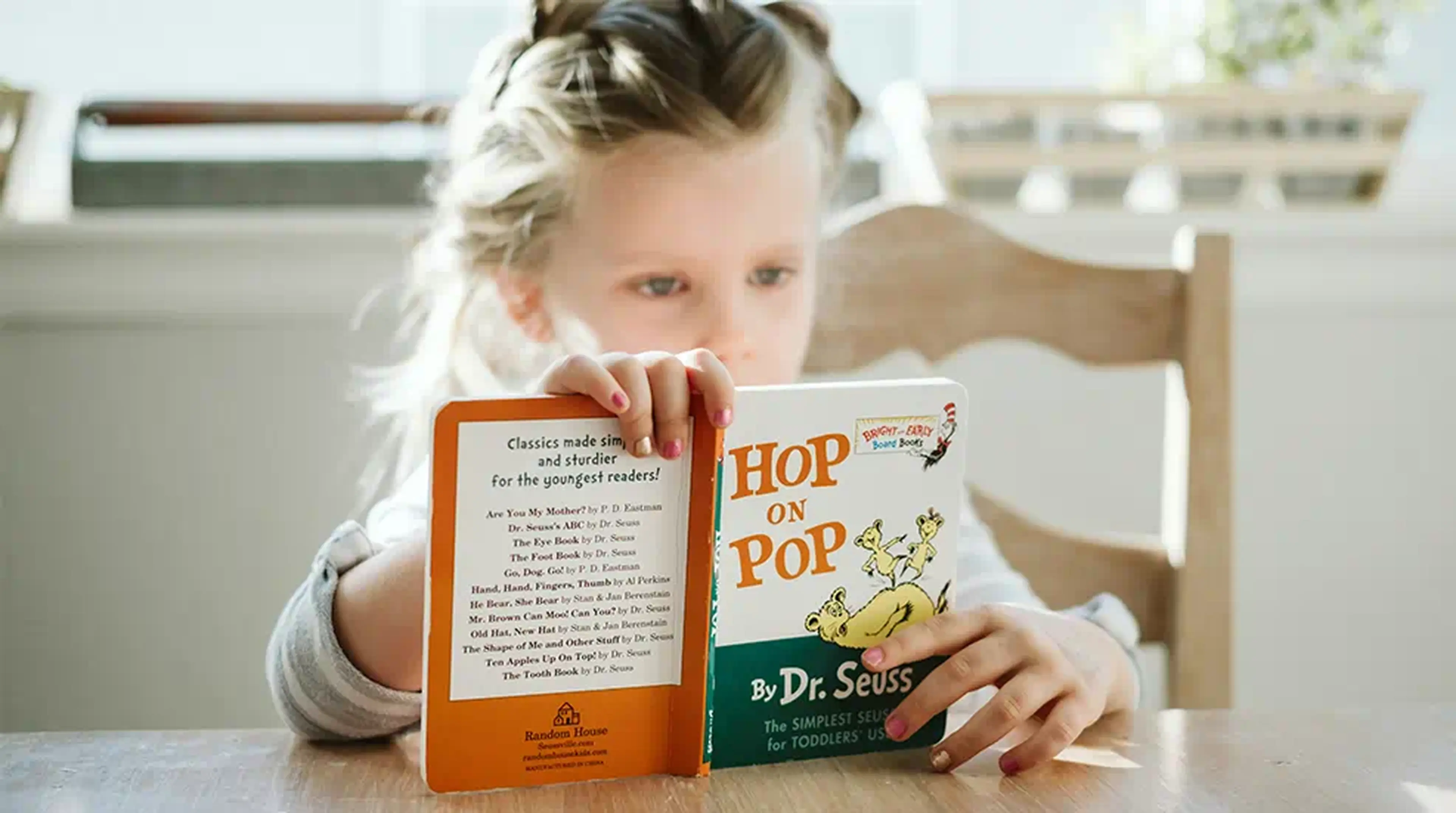 Child reading "Hop on Pop" by Dr. Seuss at a wooden table