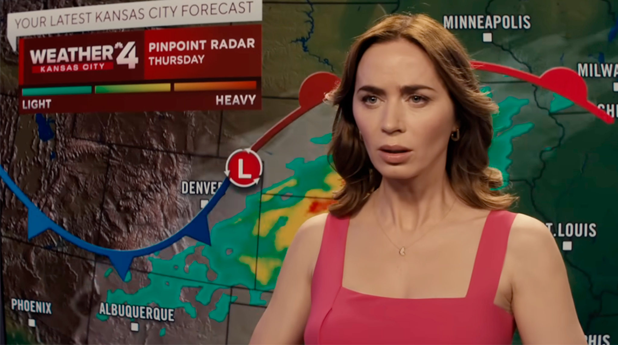 A weather presenter in a pink dress stands in front of a weather map showing storm systems over Kansas City and surrounding areas.