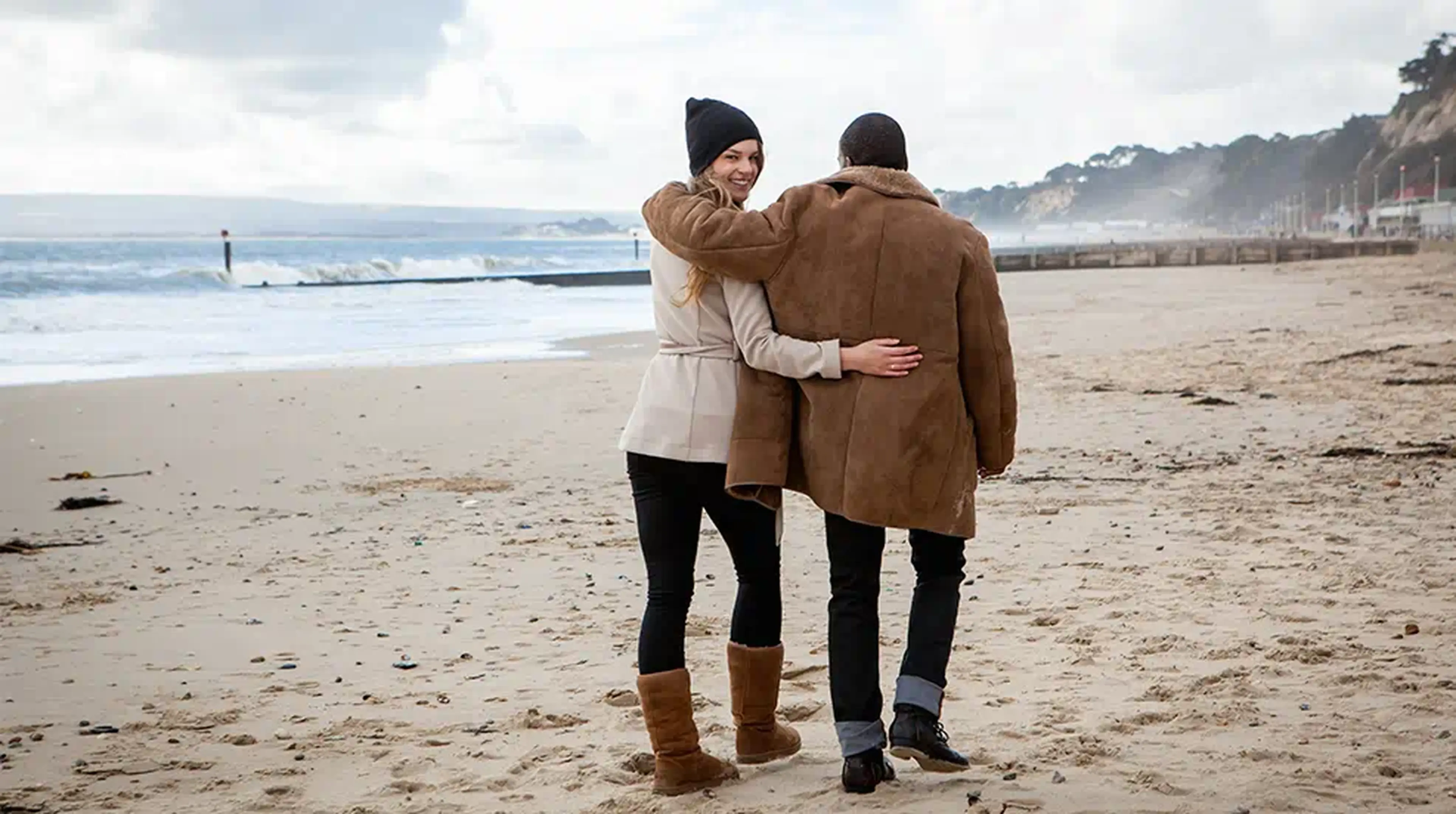 A couple walks along a sandy beach on a cloudy day