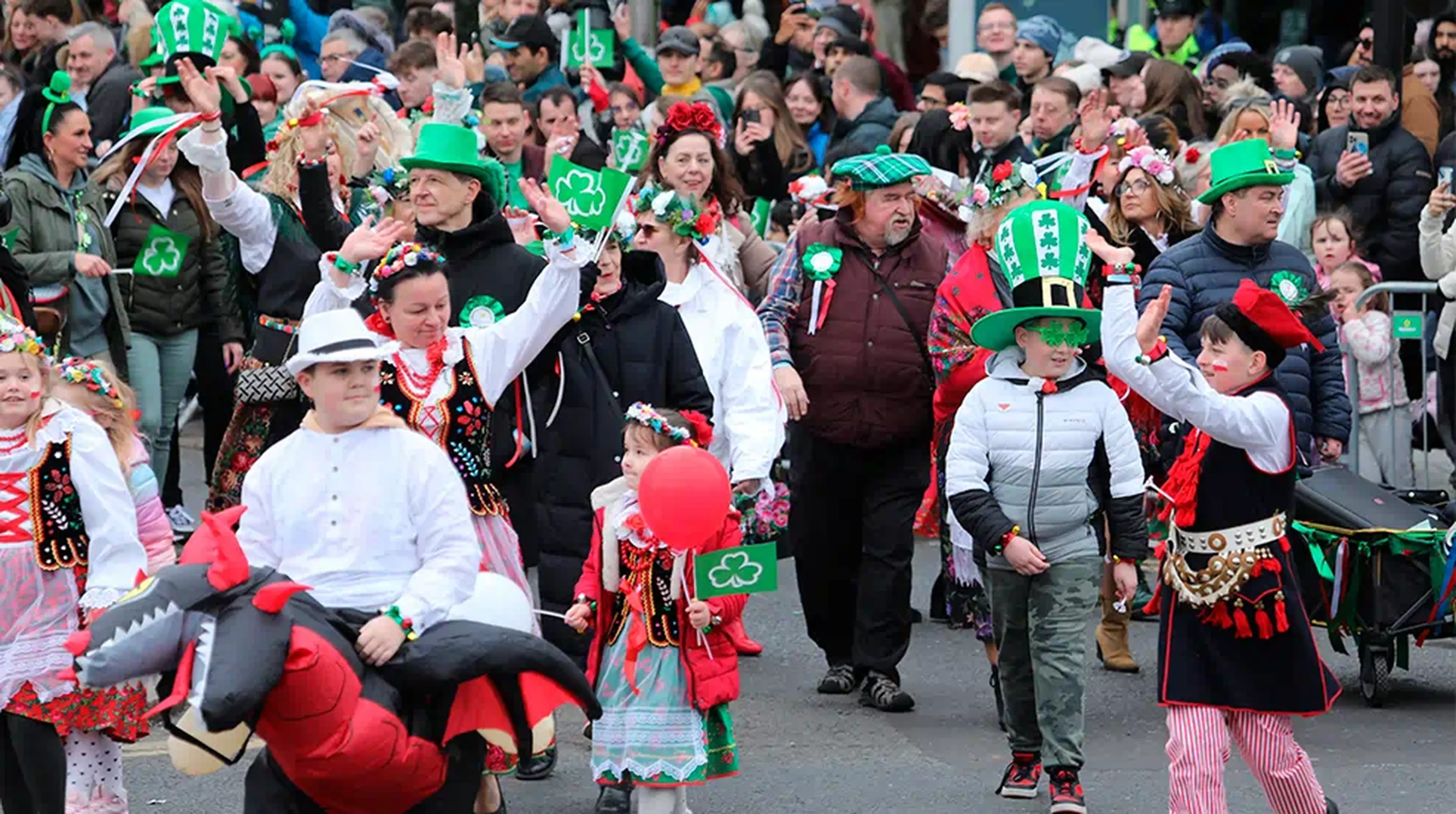 A festive crowd in colourful costumes and green hats celebrates outdoors