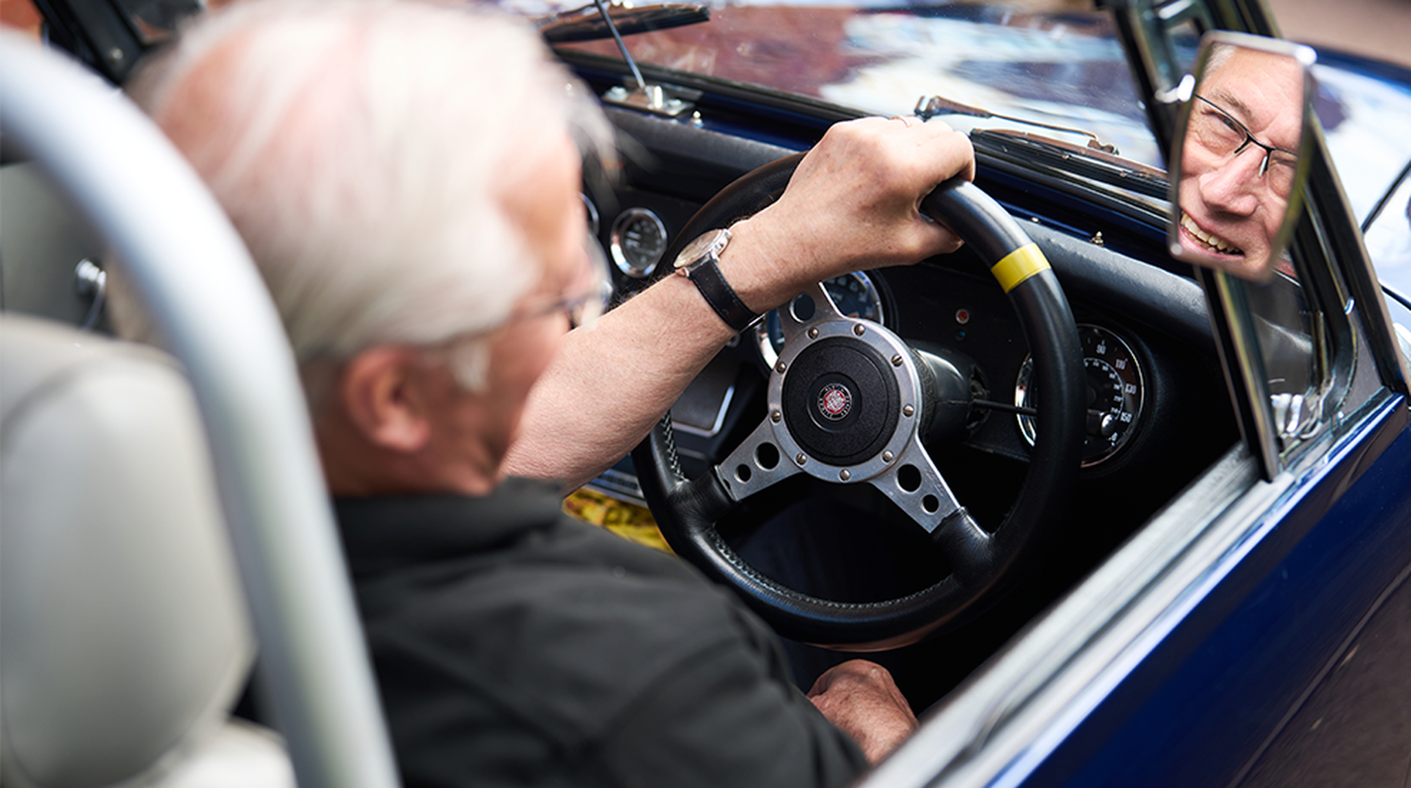 Mike Harrison smiling into reflection of car wing mirror