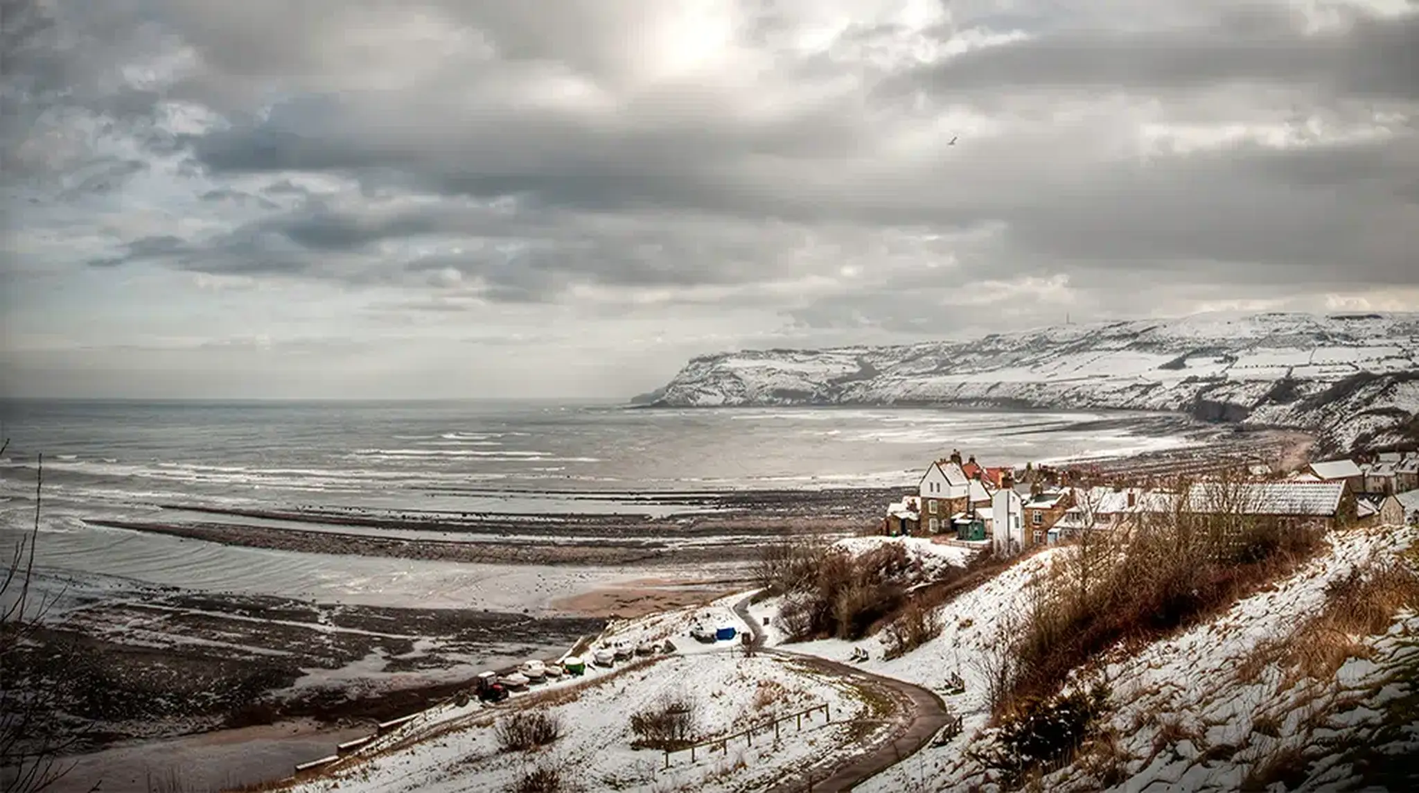 Snow-covered coastal village with cliffs and a winding road