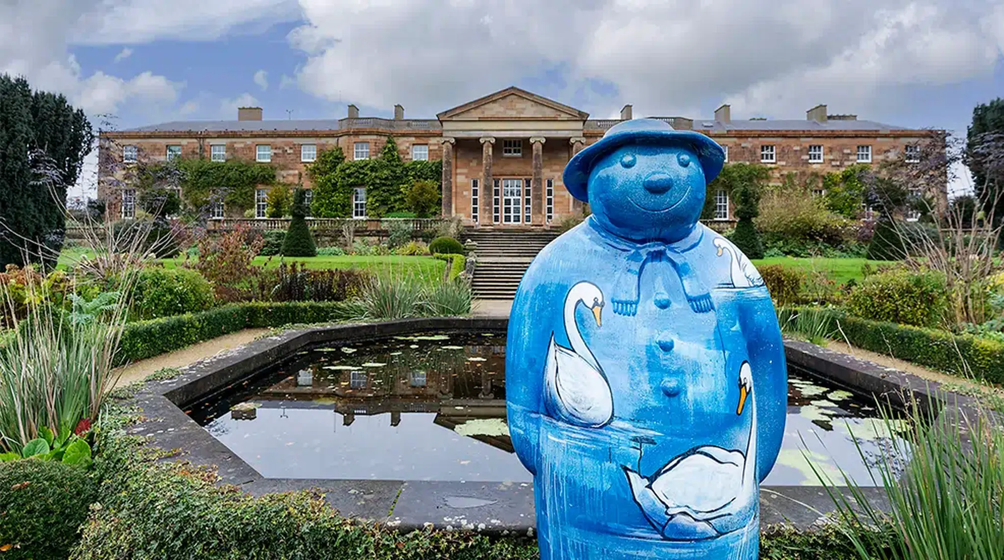 A blue ceramic figure stands in front of a rectangular pond at Hillsborough Castle and Gardens.