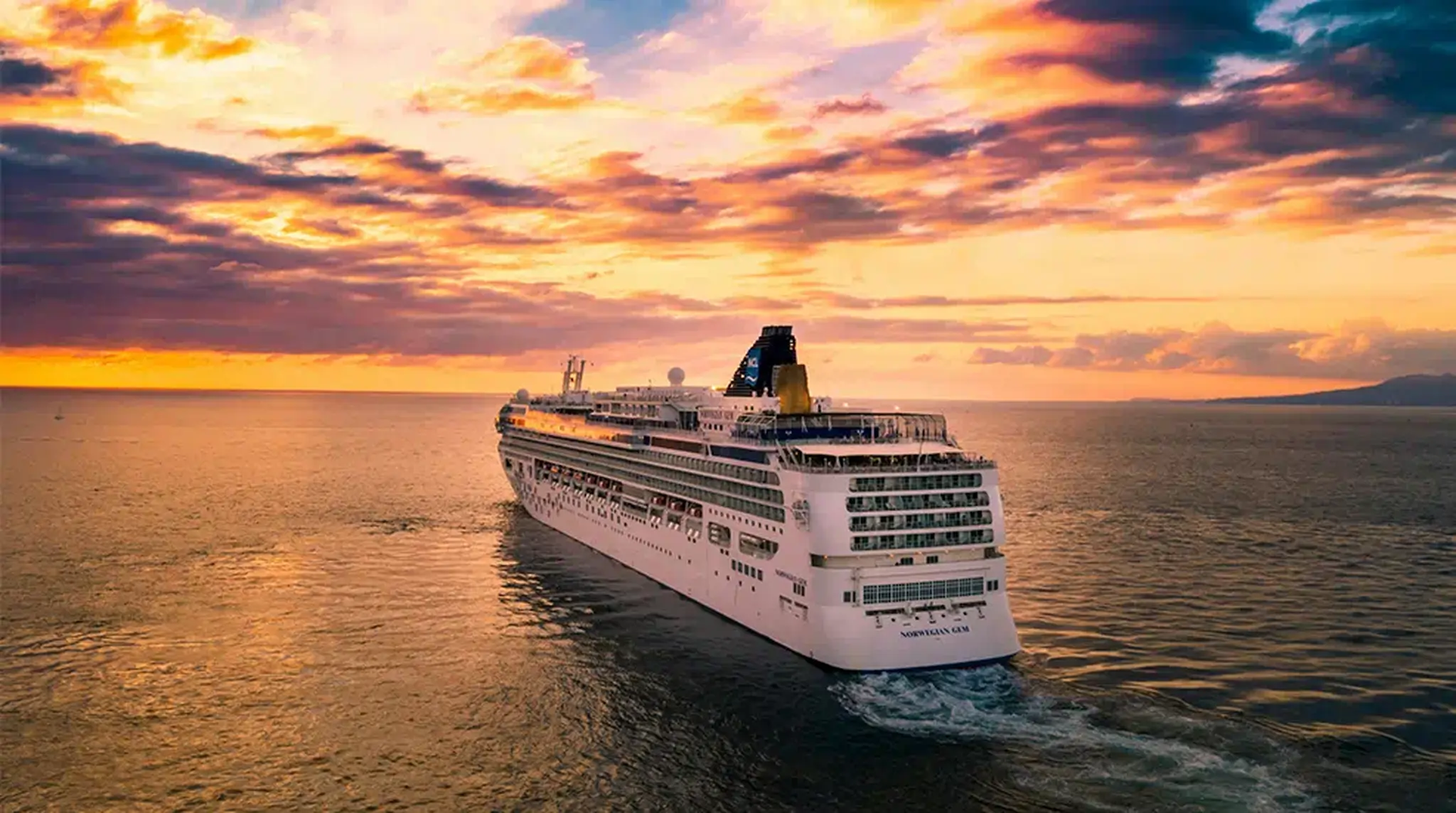 A large cruise ship sails on calm waters under a vibrant sunset sky