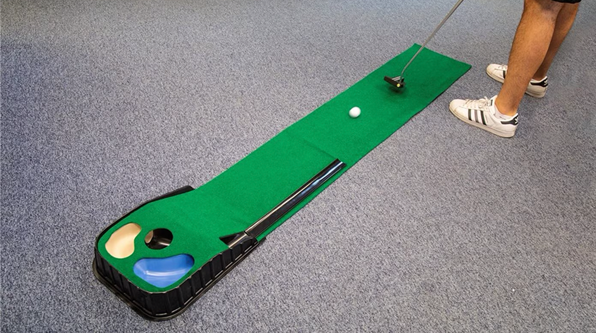 Person playing mini golf indoors on a green putting mat