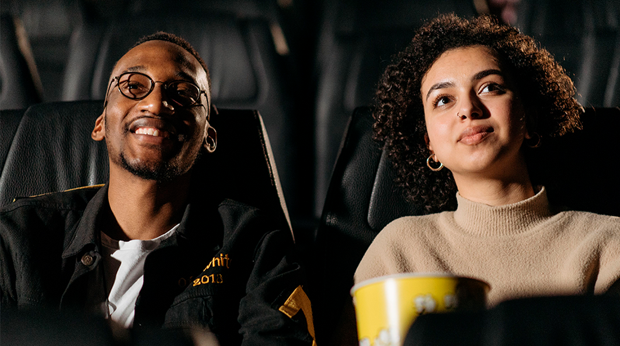 Smiling young couple watching a movie in theater, sharing popcorn.