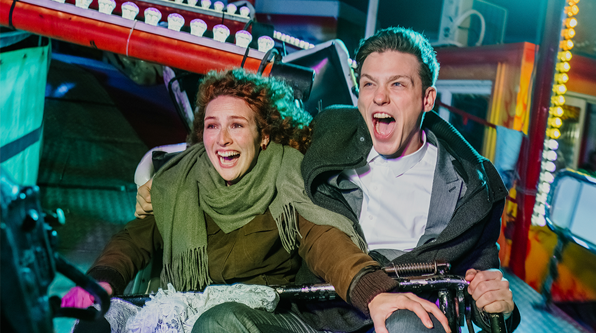 Young couple screaming while riding roller coaster at fairground