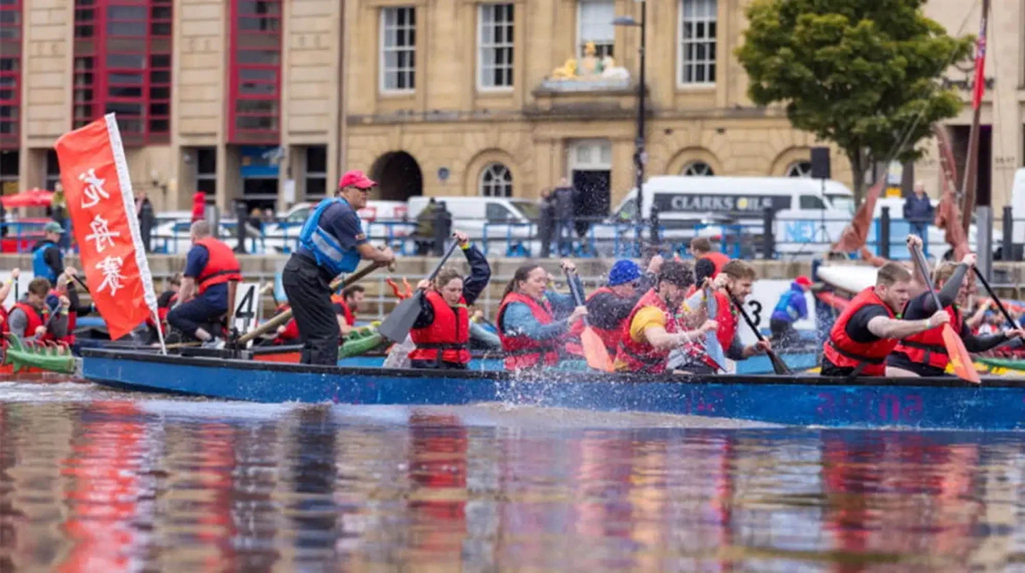People rowing in a dragon boat race on a river, wearing life jackets