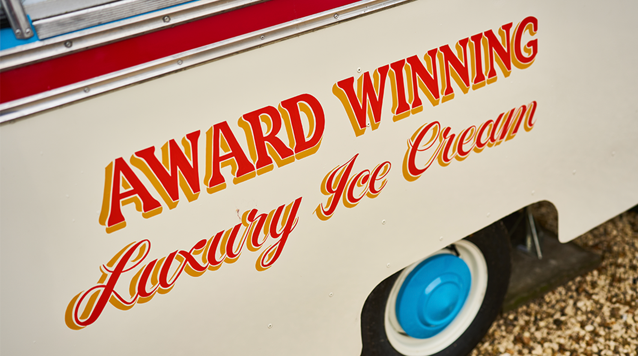 Side of an ice cream truck with bold red and yellow text: "Award Winning Luxury Ice Cream," and a visible blue wheel.