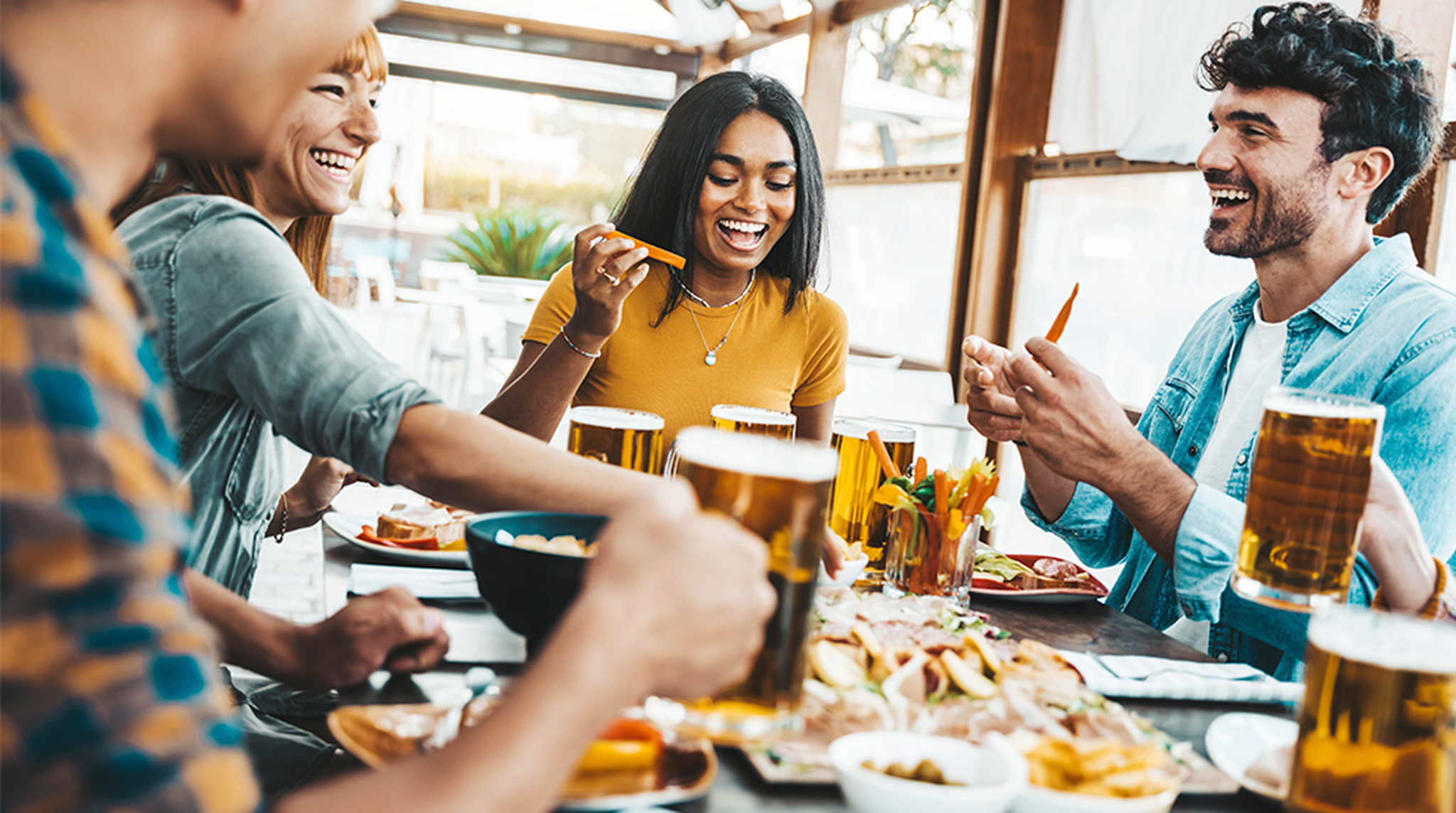 Multiethnic happy friends drinking beer glasses sitting at brewery pub restaurant table