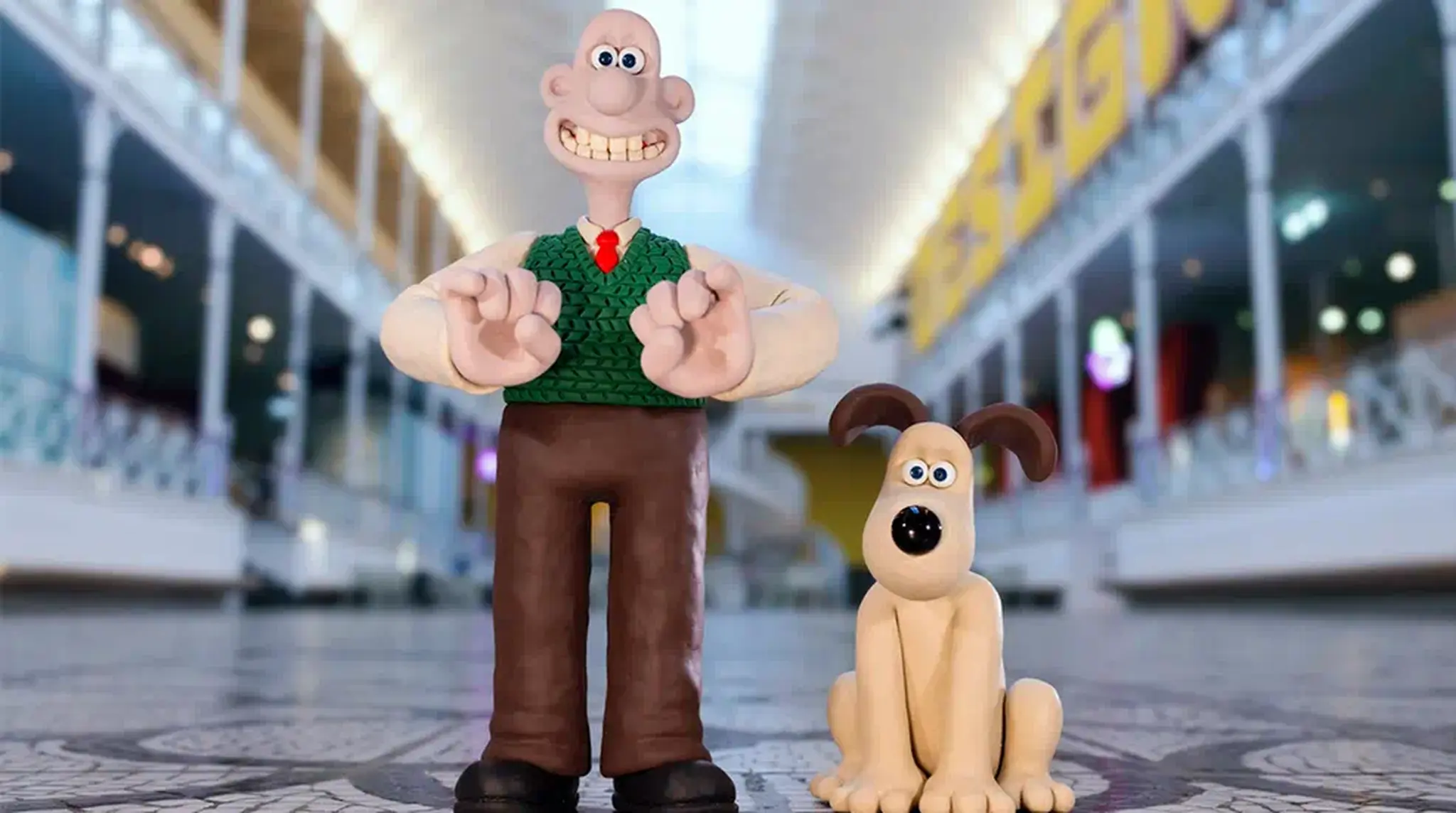 Clay figures of a smiling man in a green vest and a dog. Wallace and Gromit
