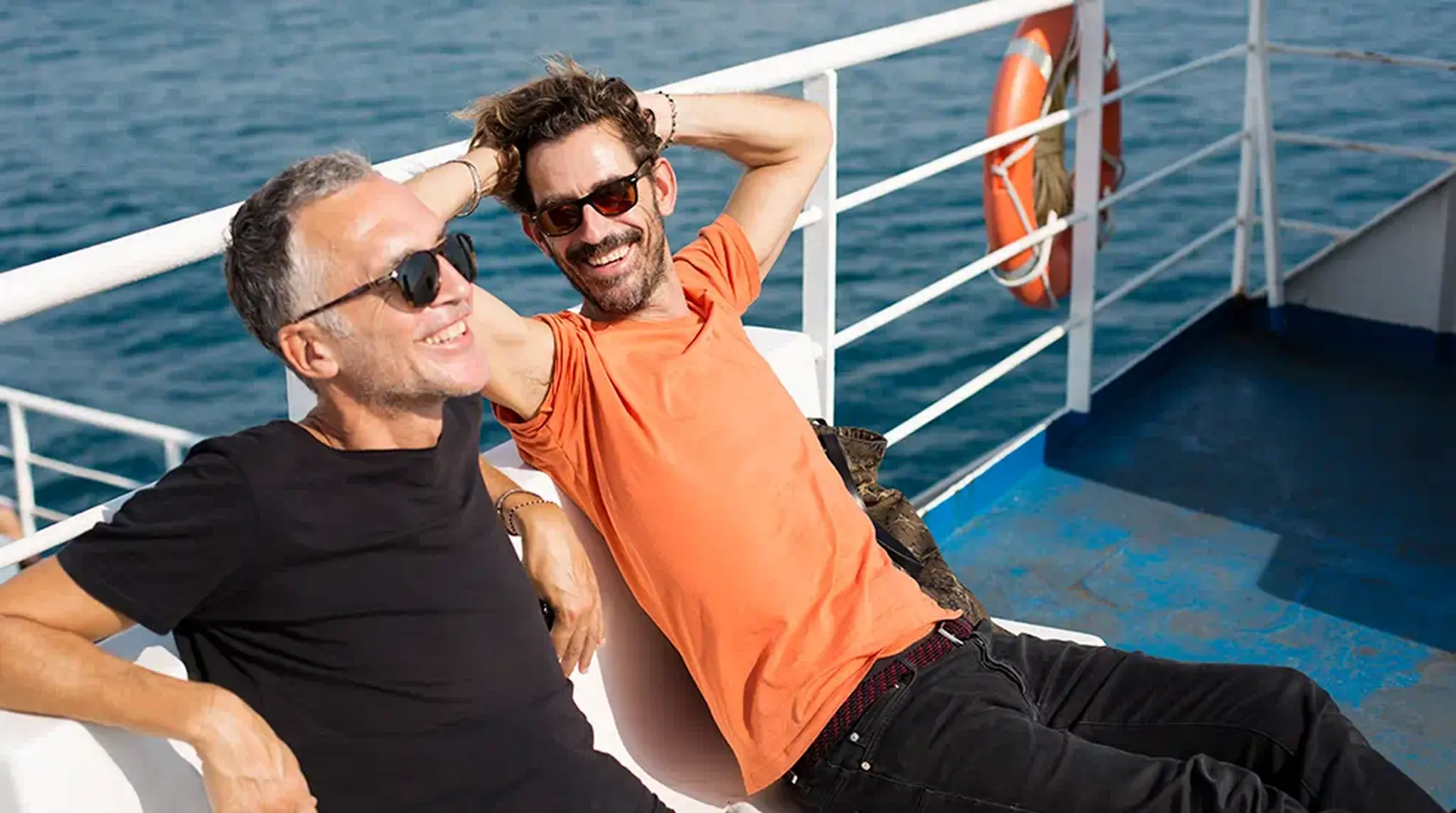 Two men in sunglasses relax and smile on a boat deck