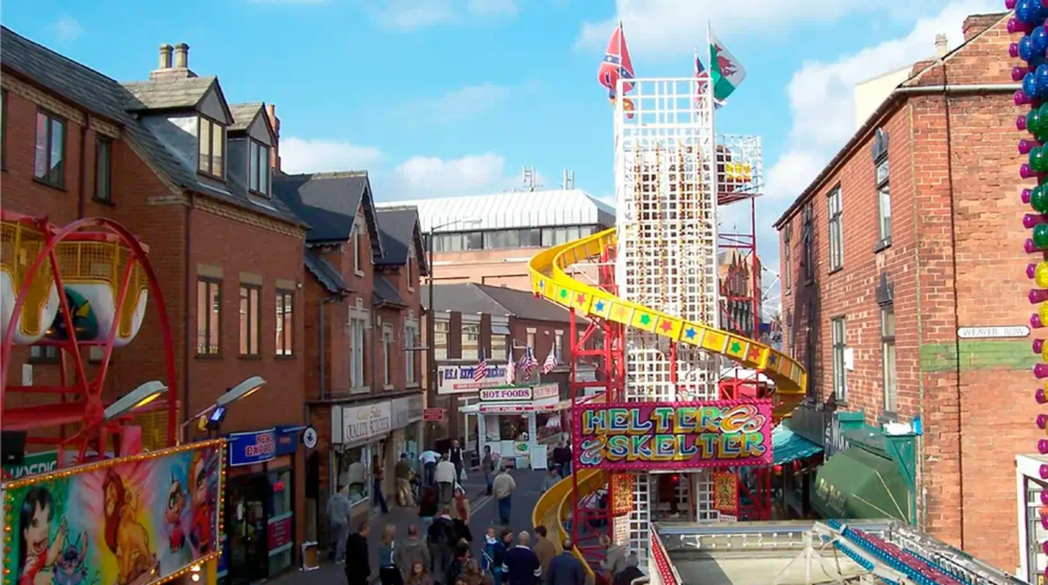 A bustling street fair with a colourful helter-skelter slide, vibrant stalls, and crowds