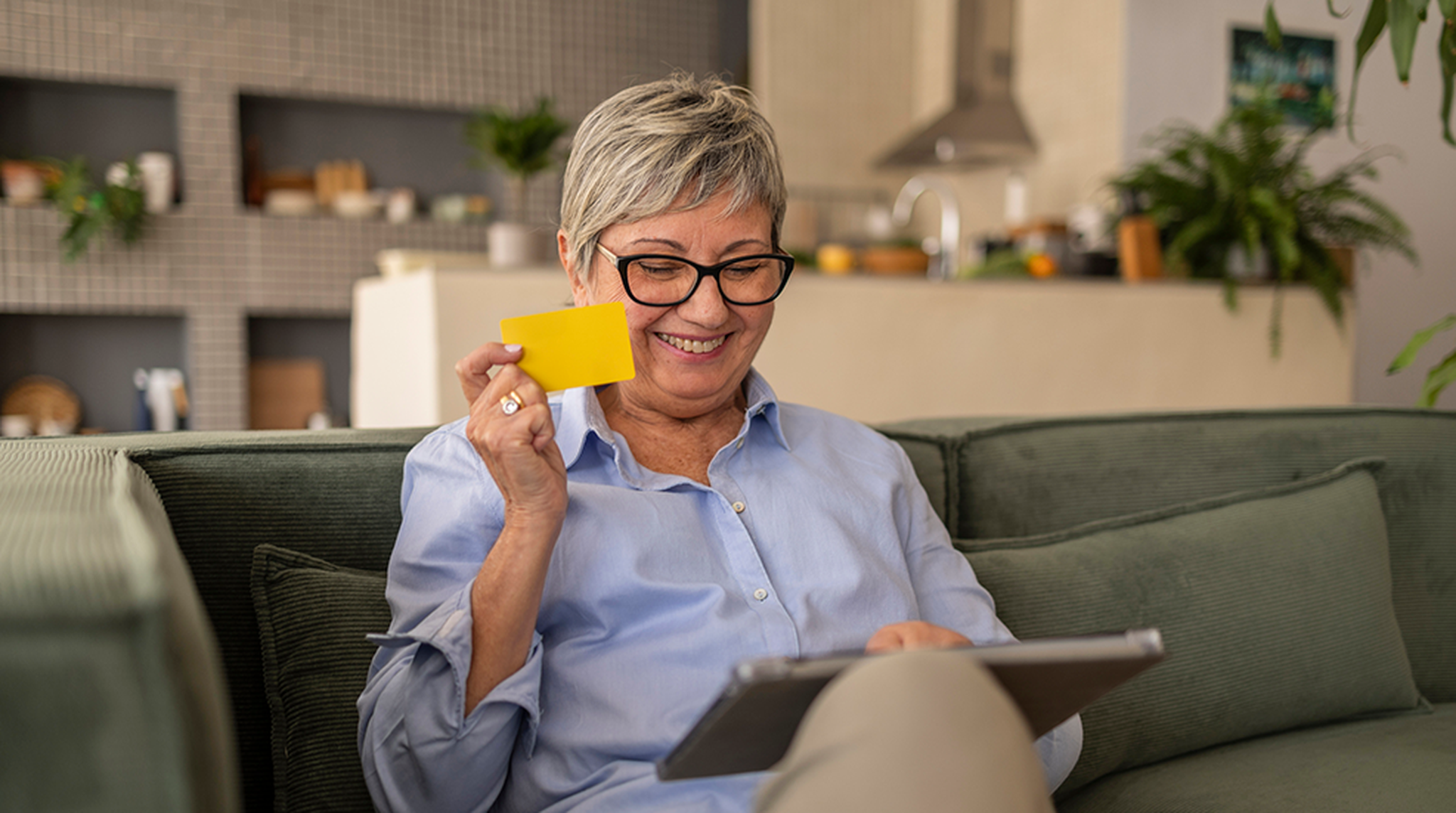 Senior woman happily shopping online with a credit card and digital tablet at home