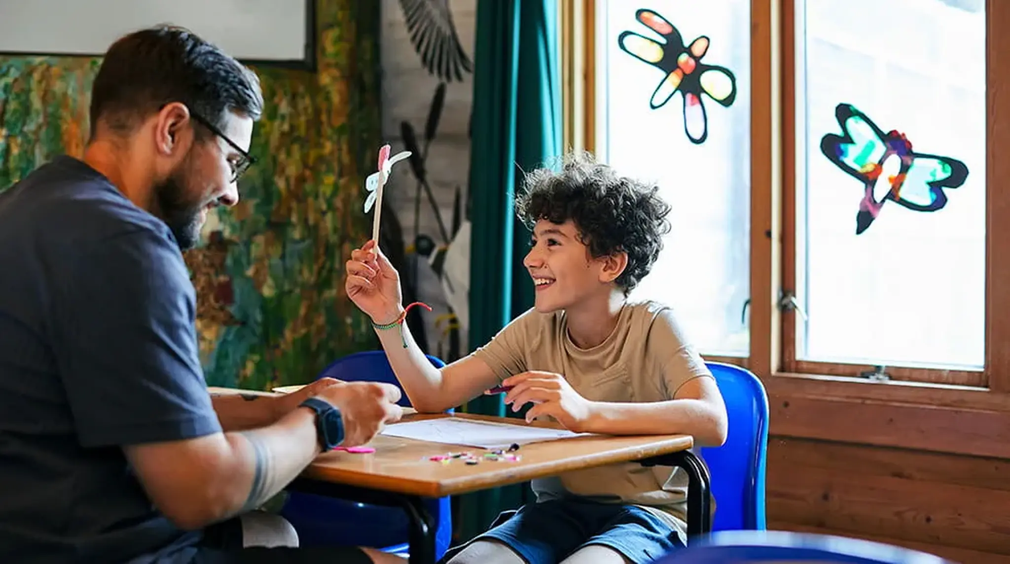 A man and a smiling boy engage in a craft activity at a table