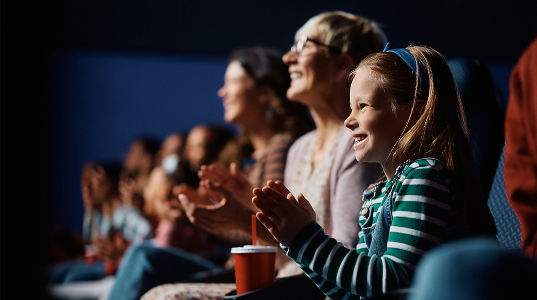 Focus on a young girl smiling and clapping hands in cinema with rest of the audience blurred