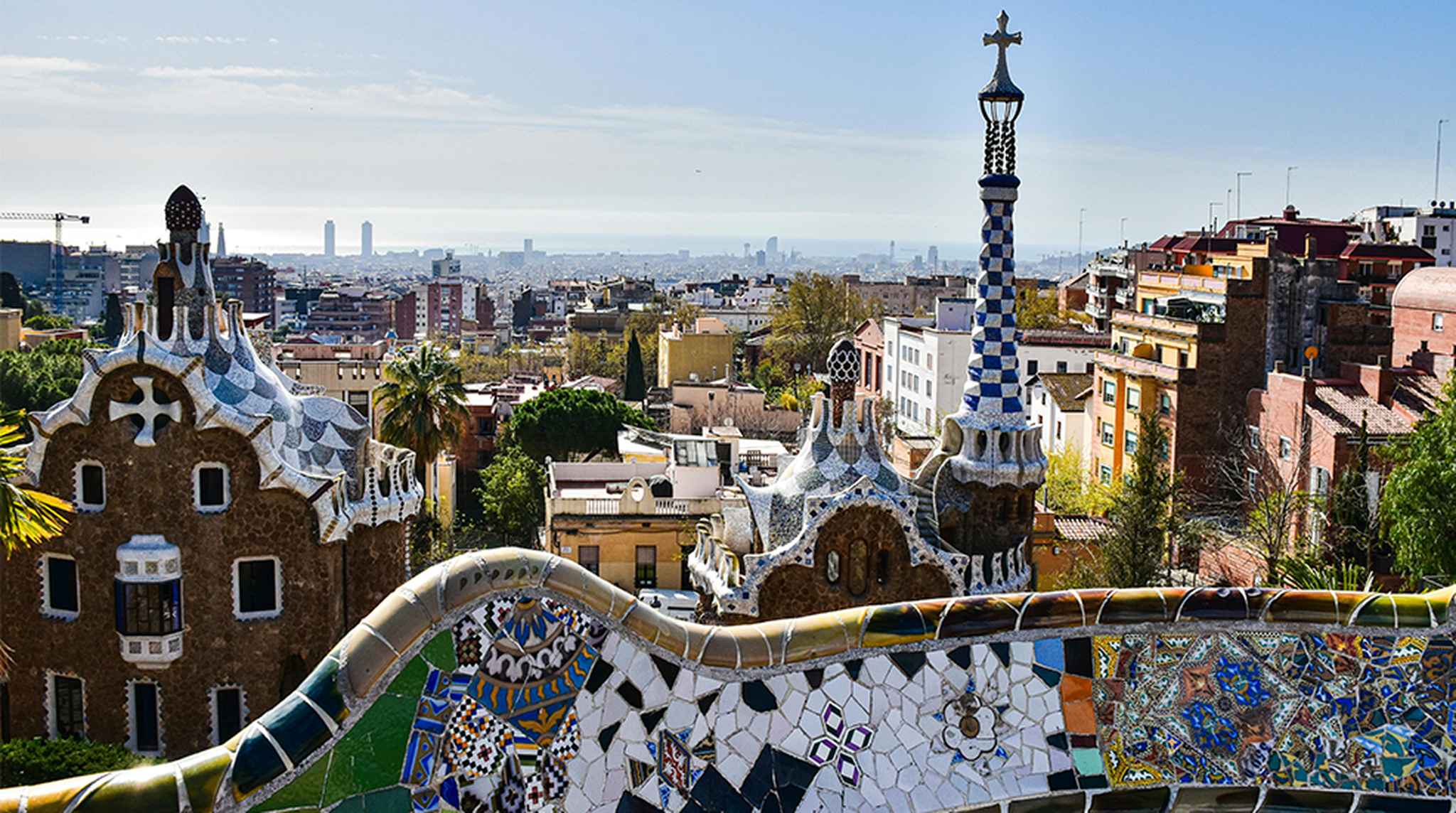 Gaudí's iconic mosaic architecture in Park Güell with a view of Barcelona's cityscape.