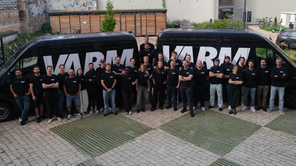 Team der VARM GmbH vor zwei Firmenfahrzeugen mit VARM-Logo. Gruppenfoto der Mitarbeiter am Standort Berlin, spezialisiert auf Einblasdämmung und Gebäudedämmung.