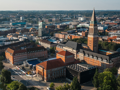 Luftaufnahme des Kieler Rathauses mit Turm und Rathausplatz, im Hintergrund die Förde und Teile der Innenstadt bei klarem Wetter.