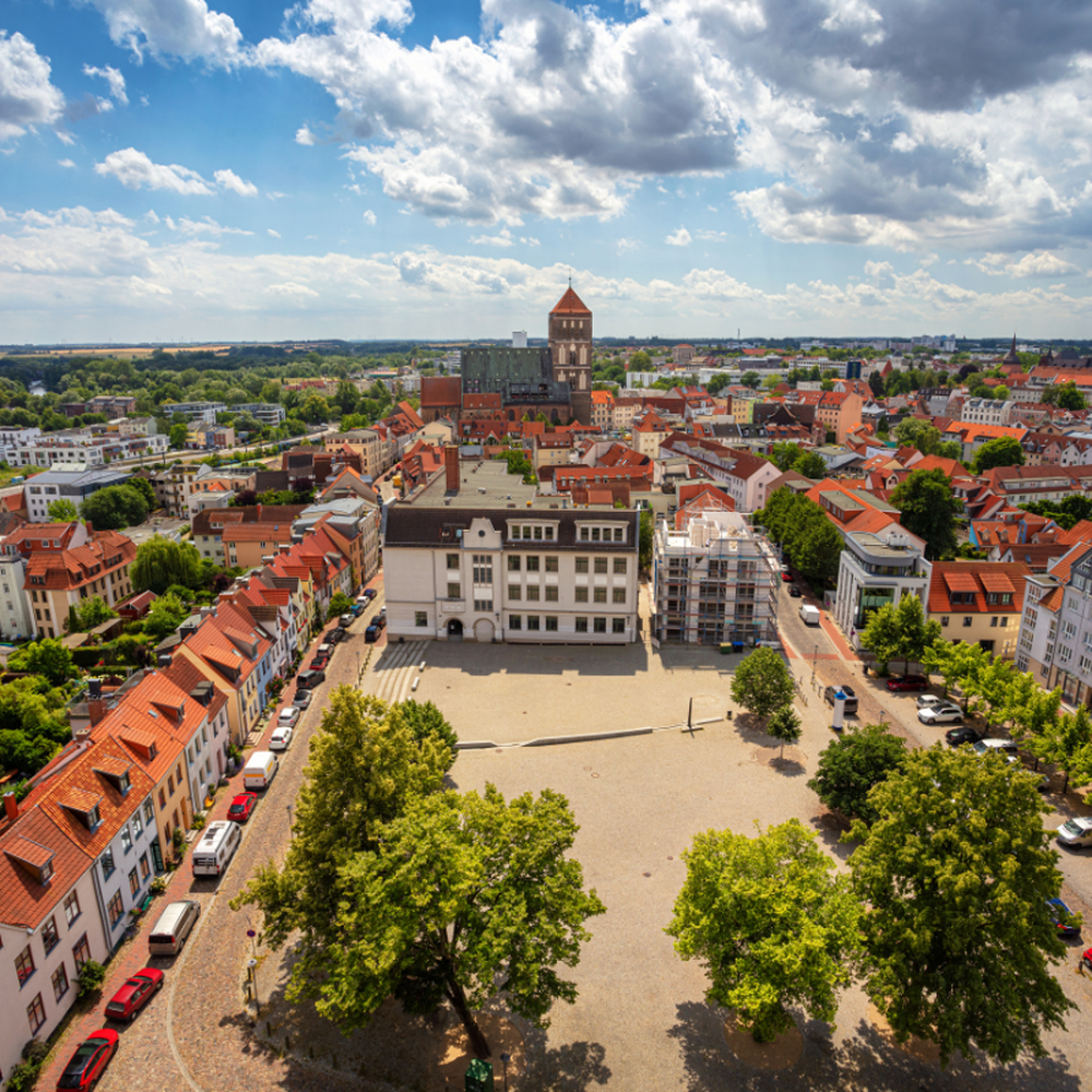 Luftaufnahme der Altstadt von Rostock mit dem Neuen Markt, historischen Gebäuden und der Marienkirche im Hintergrund unter leicht bewölktem Himmel.