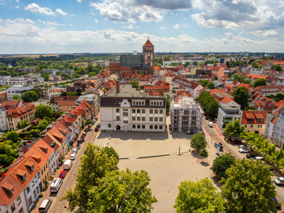 Luftaufnahme der Altstadt von Rostock mit dem Neuen Markt, historischen Gebäuden und der Marienkirche im Hintergrund unter leicht bewölktem Himmel.