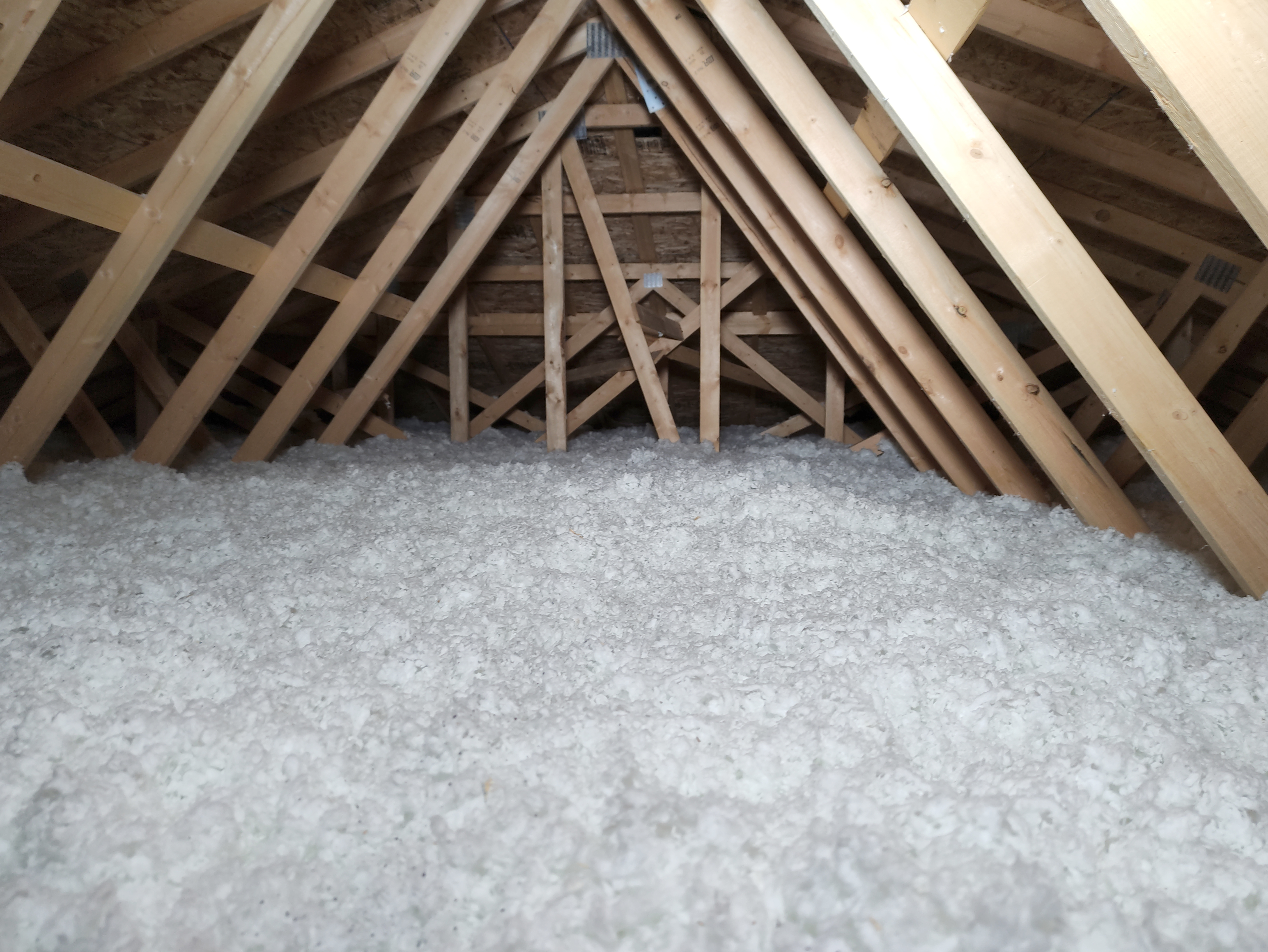 Dämmung eines Dachbodens mit weißer, flockiger Einblasdämmung zwischen den offenen Holzsparren eines nicht ausgebauten Dachstuhls.