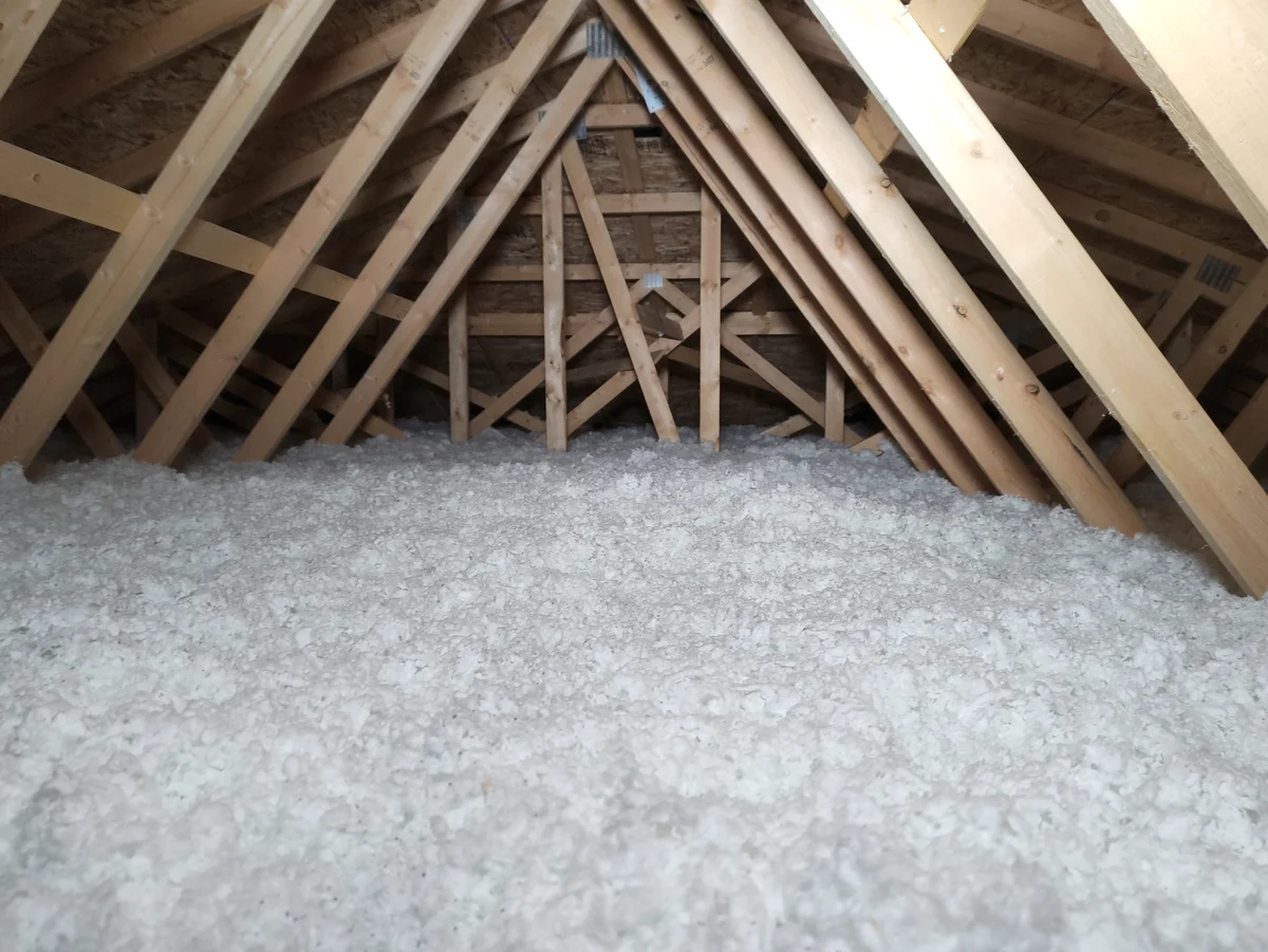 Dämmung eines Dachbodens mit weißer, flockiger Einblasdämmung zwischen den offenen Holzsparren eines nicht ausgebauten Dachstuhls.