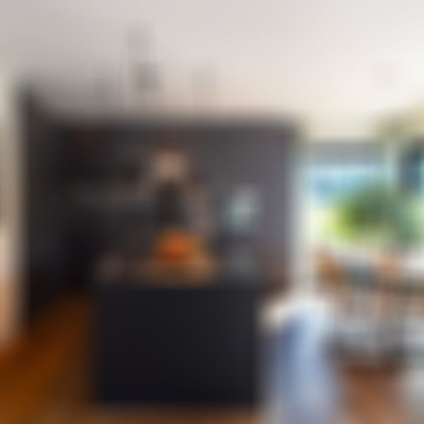 Moderne Küche mit dunklen Schränken, Kochinsel mit Hängelampen, Esstisch aus Holz, großen Fenstern, Vorhängen und einer Topfpflanze.