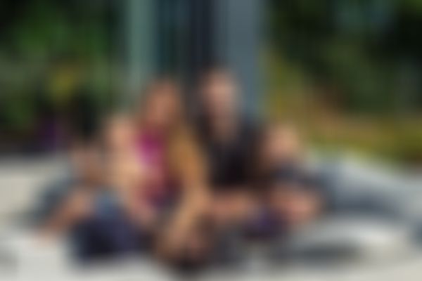 Lächelnde vierköpfige Baufamilie, die auf einem Sofa im Freien sitzt, wobei die Eltern ihre kleinen Kinder im Arm halten, umgeben von Grün an einem sonnigen Tag.