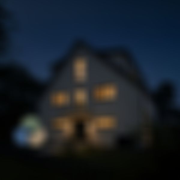 ernes zweigeschossiges Haus bei Nacht mit warm beleuchteten Fenstern und stimmungsvoll inszenierter Außenbeleuchtung, umgeben von Bäumen und üppigem Grün