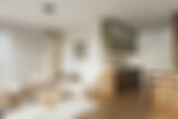 Modernes Wohn- und Esszimmer mit beigem Sofa, rundem Couchtisch, Pendelleuchten und Holzakzenten. Großes Fenster mit transparenten Vorhängen.