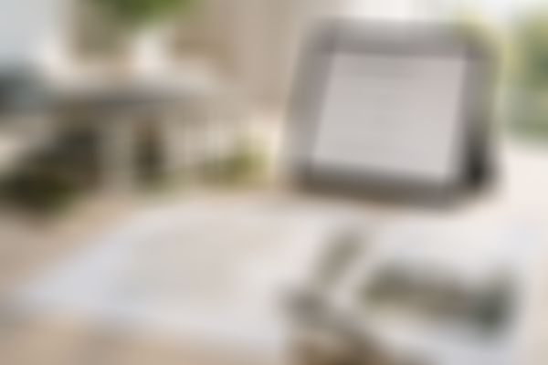 Ein Musterhaus neben einem Tablet, auf dem Finanzierungsmöglichkeiten angezeigt werden, mit Unterlagen und einem Stift auf dem Tisch.