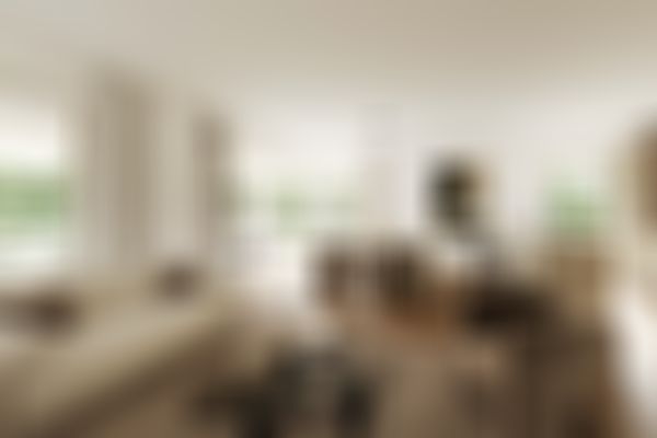 Geräumiger Wohn-Essbereich mit beigen Sofas, einem Couchtisch aus Glas, einer Esszimmergarnitur, abstrakten Wandbildern und großen Fenstern mit Blick auf den Garten.