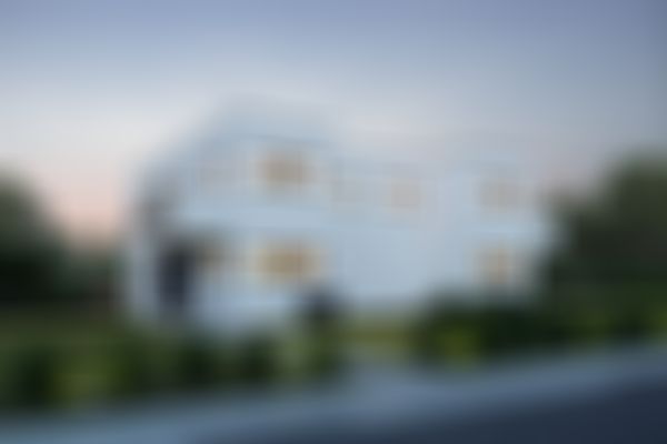 Ein modernes, weißes, kubisches Haus mit großen Fenstern, einem hell erleuchteten Innenraum und einem gepflegten Rasen, vor dem Hintergrund eines Abendhimmels und umgeben von Grünflächen.