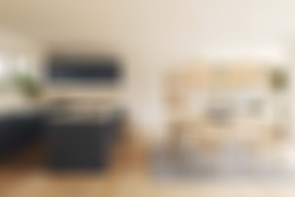 Moderner Koch- und Essbereich mit dunkelblauen Schränken, Holzboden, einer großen Kücheninsel, viel Tageslicht und Pendelleuchten aus Korbgeflecht über einem Holztisch.