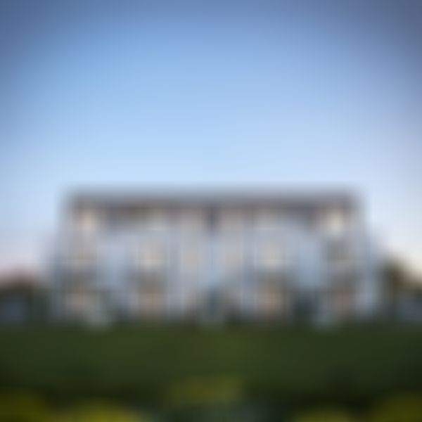 Modernes dreistöckiges Gebäude mit großen Fenstern und Balkonen, umgeben von viel Grün, unter einem klaren Abendhimmel.