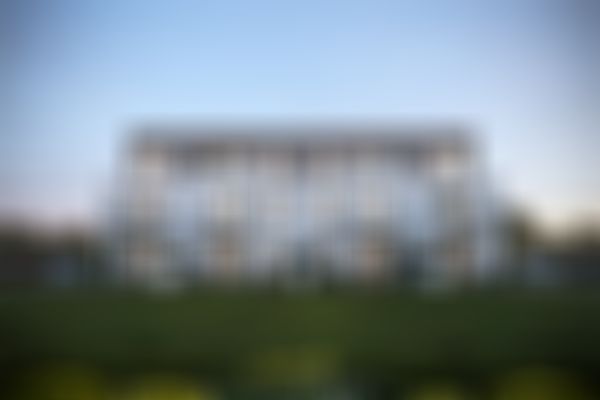 Modernes dreistöckiges Gebäude mit großen Fenstern und Balkonen, umgeben von viel Grün, unter einem klaren Abendhimmel.