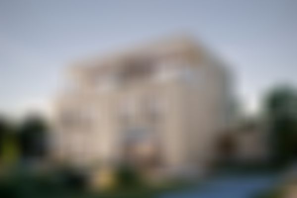 Modernes dreigeschossiges Haus mit großen Fenstern, Balkonen und einer Terrasse, umgeben von einem liebevoll gestalteten Garten und Bäumen in der Abenddämmerung.