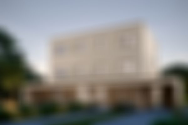 Modernes dreigeschossiges beigefarbenes Gebäude mit großen Fenstern, umgeben von üppigem Grün und einer gepflegten Zufahrt, vor einem klaren Himmel.