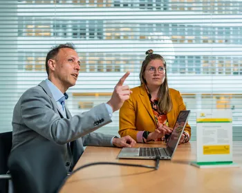 Energie consultant en klant in een zakelijk overleg over energieadvies, met laptop en presentatiemateriaal aan vergadertafel.