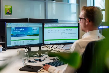 Energieconsultant van Unica analyseert marktgegevens en prijstrends voor elektriciteit op dubbele schermen binnen het Energie Management Systeem.