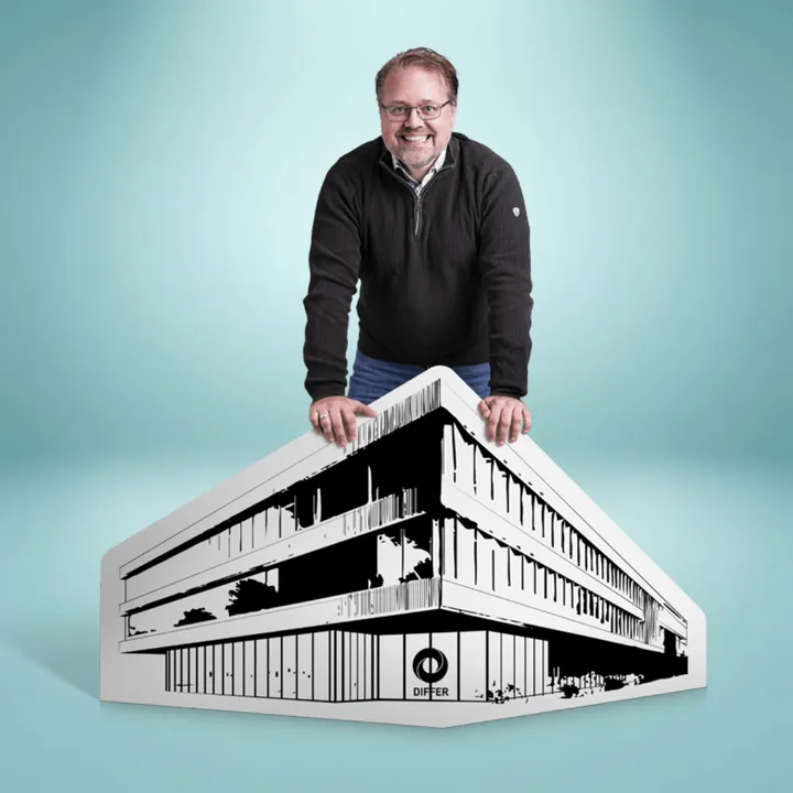 Man smiling, leaning on a large monochrome illustration of a modern building labeled "DIFER" against a light blue background.