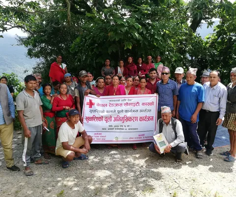 A group of people posing with a Red Cross banner outdoors, surrounded by trees and mountains.