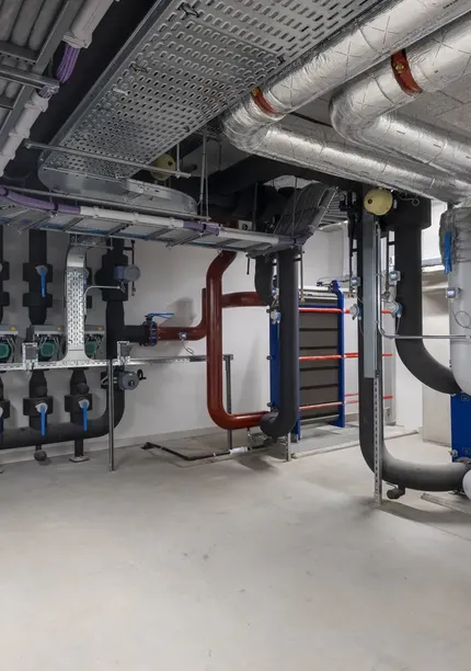 A clean, modern basement with exposed pipes, ducts, and industrial equipment, featuring insulated pipes and a neat arrangement on the walls.