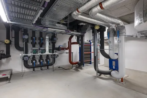 A clean, modern basement with exposed pipes, ducts, and industrial equipment, featuring insulated pipes and a neat arrangement on the walls.