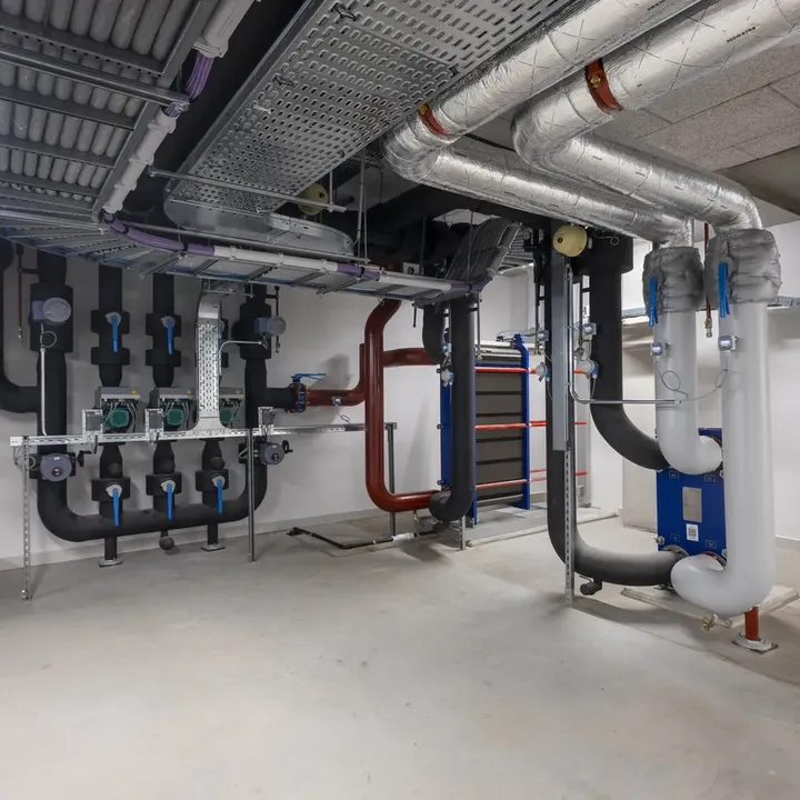 A clean, modern basement with exposed pipes, ducts, and industrial equipment, featuring insulated pipes and a neat arrangement on the walls.