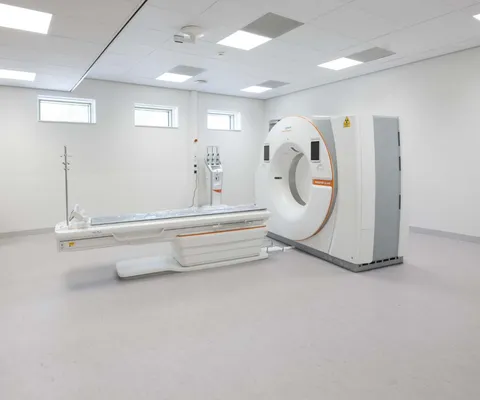 A clean, modern CT scanner in a medical imaging room with several ceiling lights and small windows.