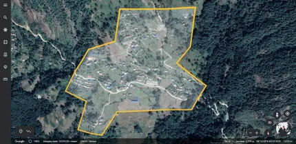 A satellite view of a mountainous, forested area with a highlighted irregular yellow boundary enclosing scattered houses and roads.
